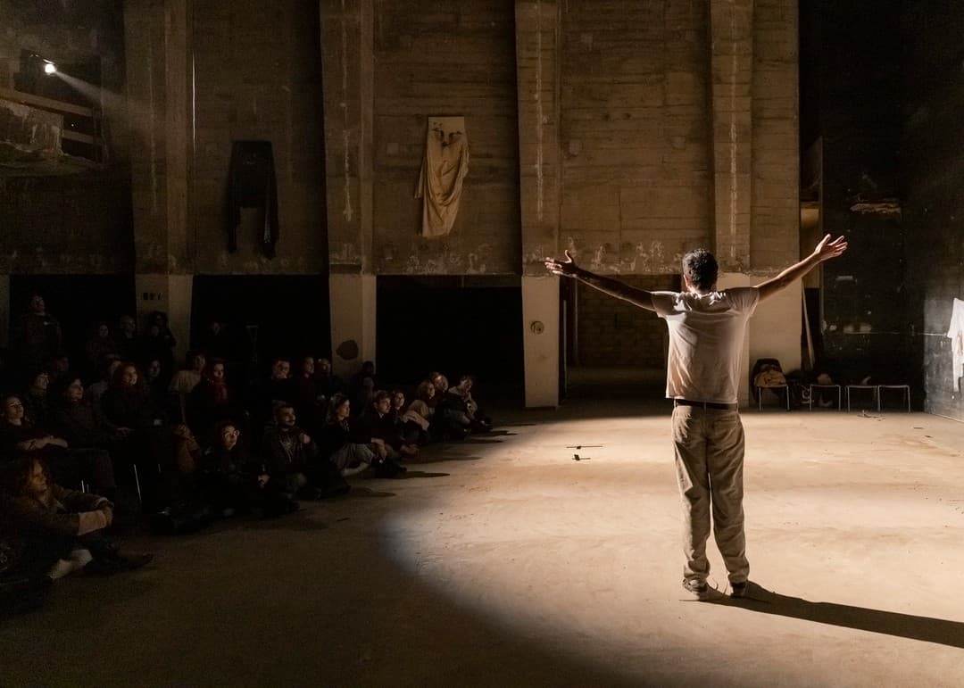 Fadi Murad, arms outstretched in a pool of light, performing to a seated audience in a raw concrete hall at Les Urbaines.